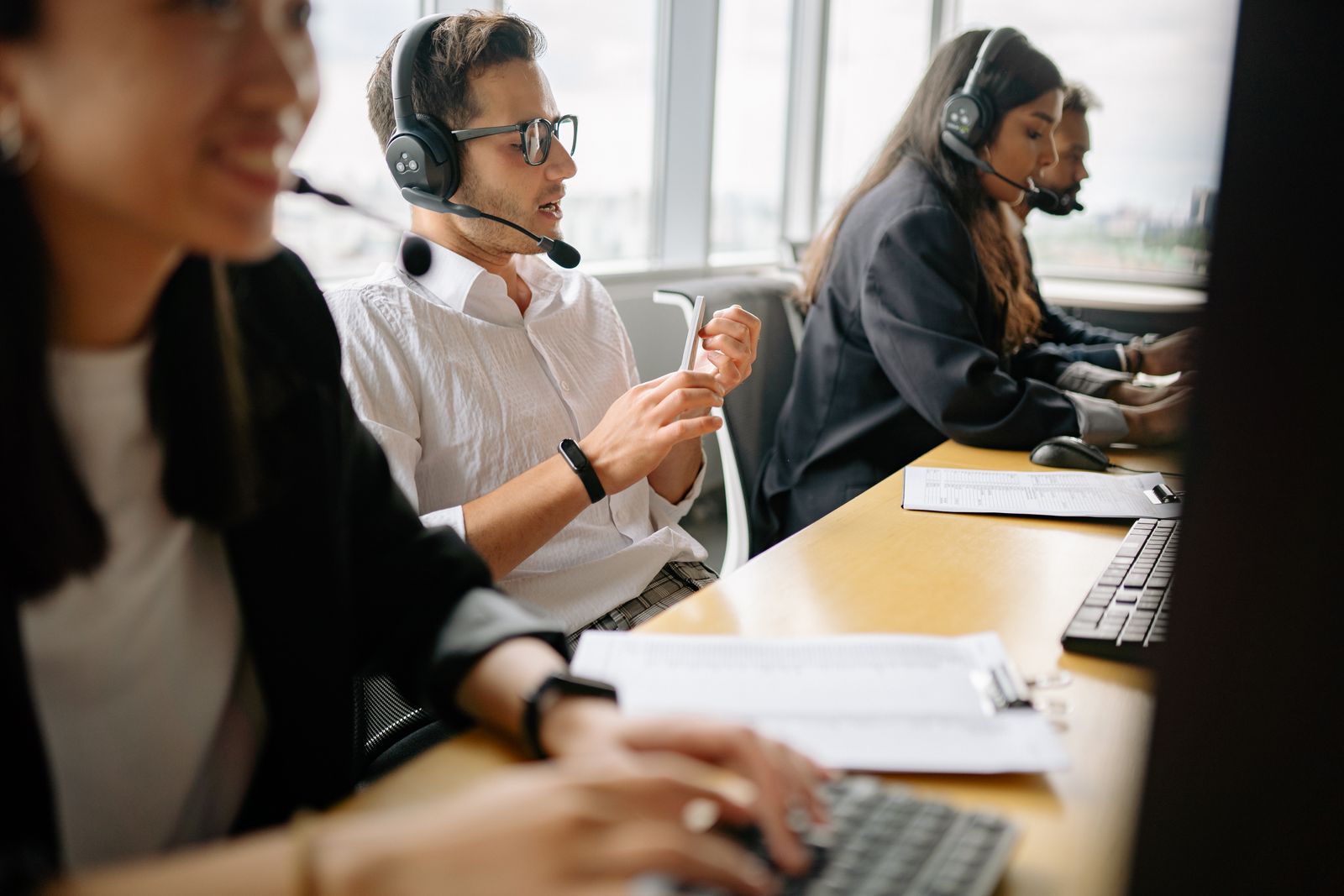 Agentes de un centro de contacto con auriculares, sentados en fila ante sus ordenadores mientras atienden llamadas.